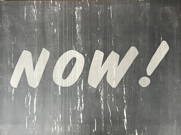 The word NOW with an exclamation mark painted in pale letters on a dark ground.